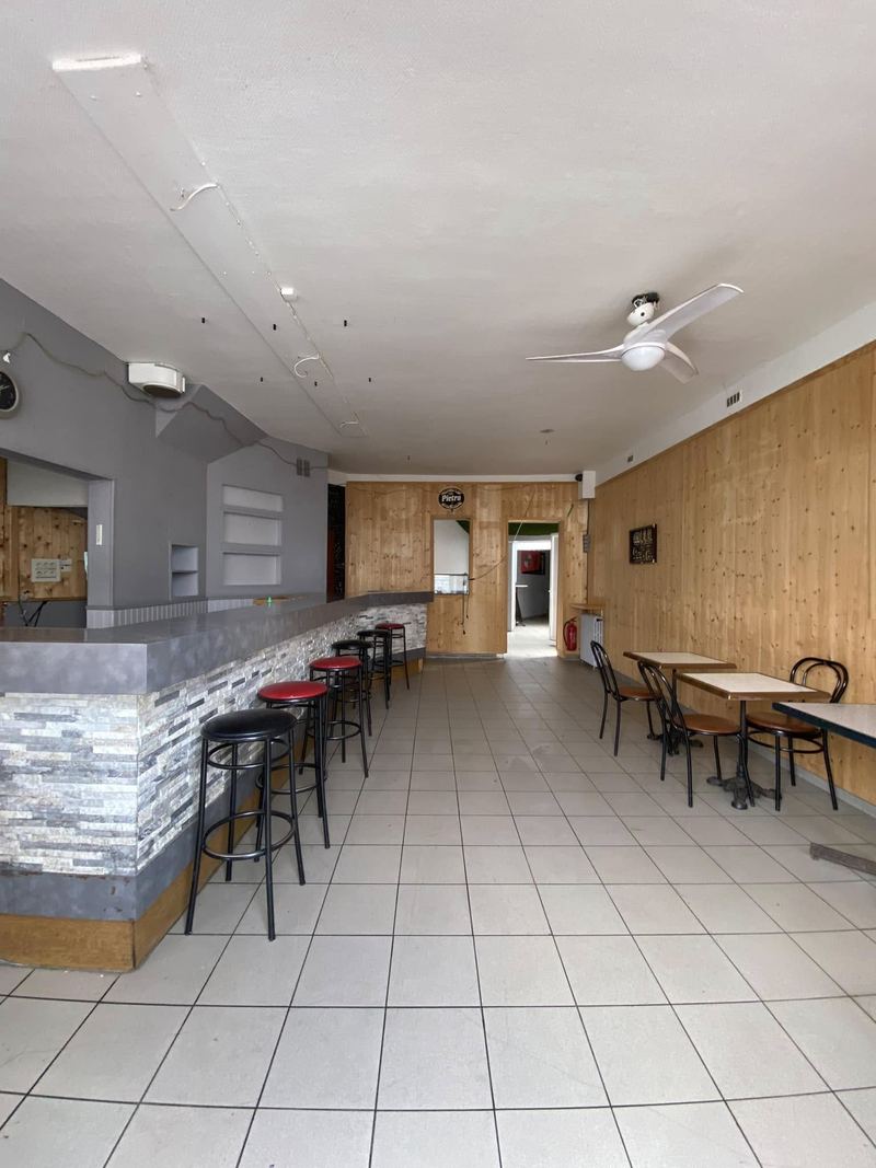 La salle vue de l'entrée : le long comptoir en parement de pierre, les tabourets, les tables bistrot, le lambris au fond
